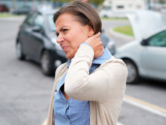 Woman holding her neck in pain after a car accident, with damaged vehicles in the background